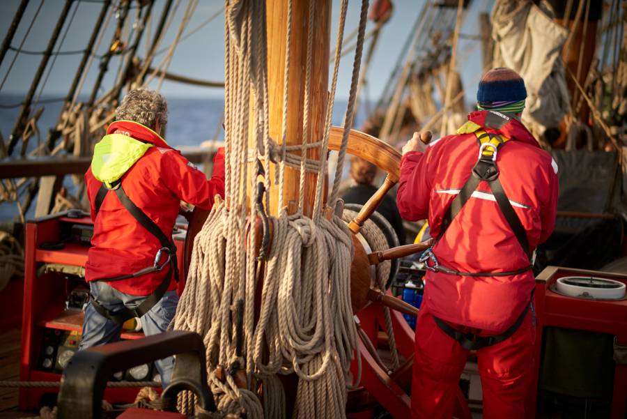 Two men standing at a ship's wheel